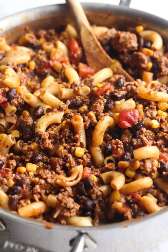 Chili mac ingredients stirred together in a large pot with a wooden spoon.