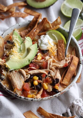 Chicken Tortilla Soup garnished with avocado, chips, sour cream, and lime