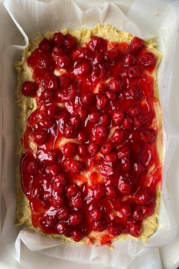 Cherry pie filling spread evenly on top of cake batter in a white baking dish.