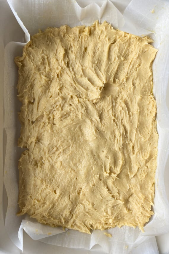 Thick vanilla cake dough pressed into a white 9x13 baking dish