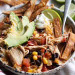 Chicken Tortilla Soup in a serving bowl with tortilla strips, avocado, a lime wedge and a spoon