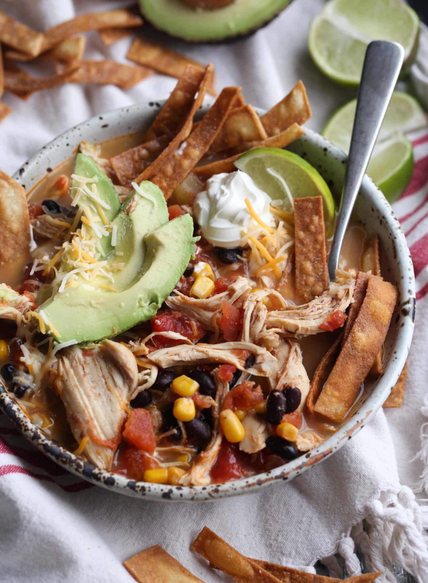 Crock Pot Chicken Tortilla Soup in a bowl with taco-style toppings on a white towel