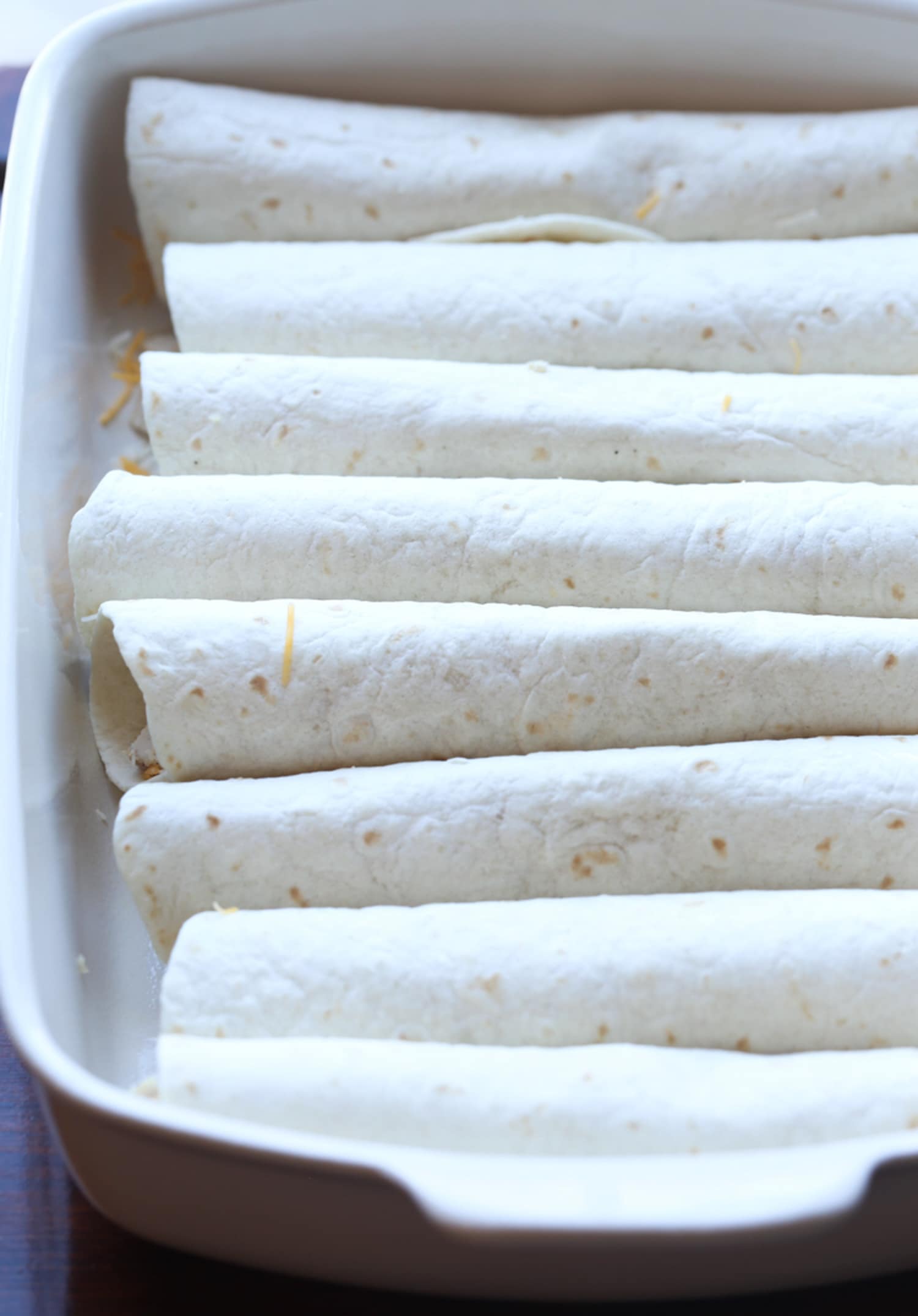 rolled up flour tortillas in a white 9x13 baking dish
