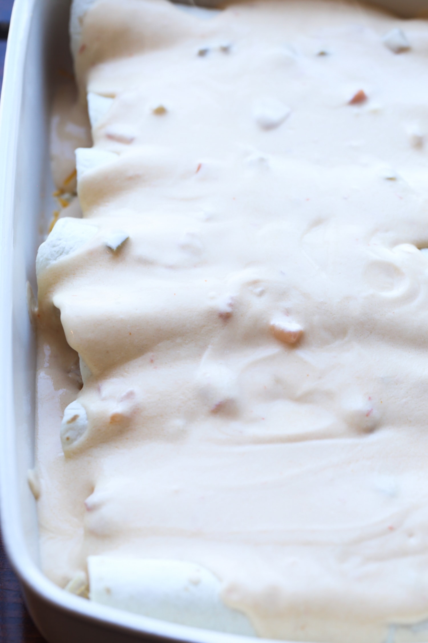 sour cream sauce on top of enchiladas in a casserole dish before going in the oven