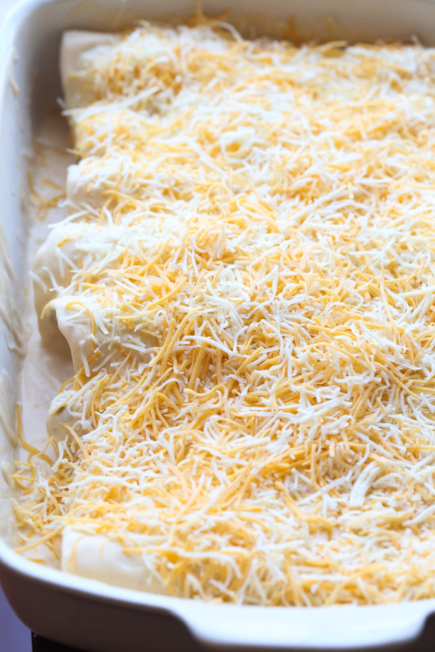 chicken filled rolled up tortillas covered in grated cheese in a baking dish