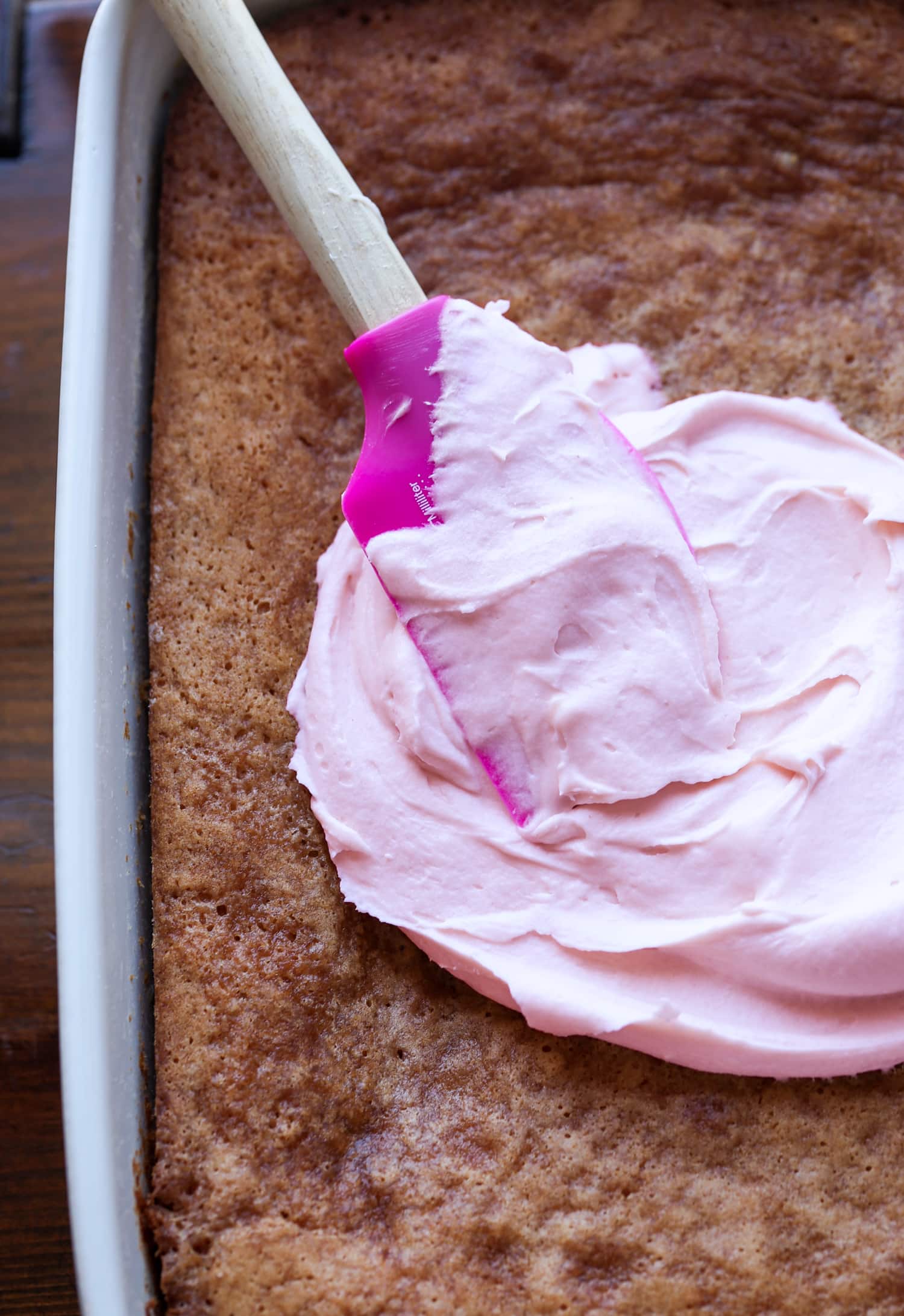 spreading strawberry cream cheese frosting onto a sheet cake in a 9x13 pan
