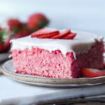 a slice of strawberry sheet cake on a plate topped with fresh strawberry slices