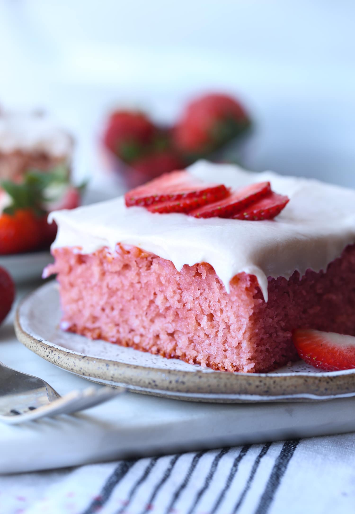 Slice of Strawberry Cake on a plate topped with cream cheese frosting and fresh strawberries
