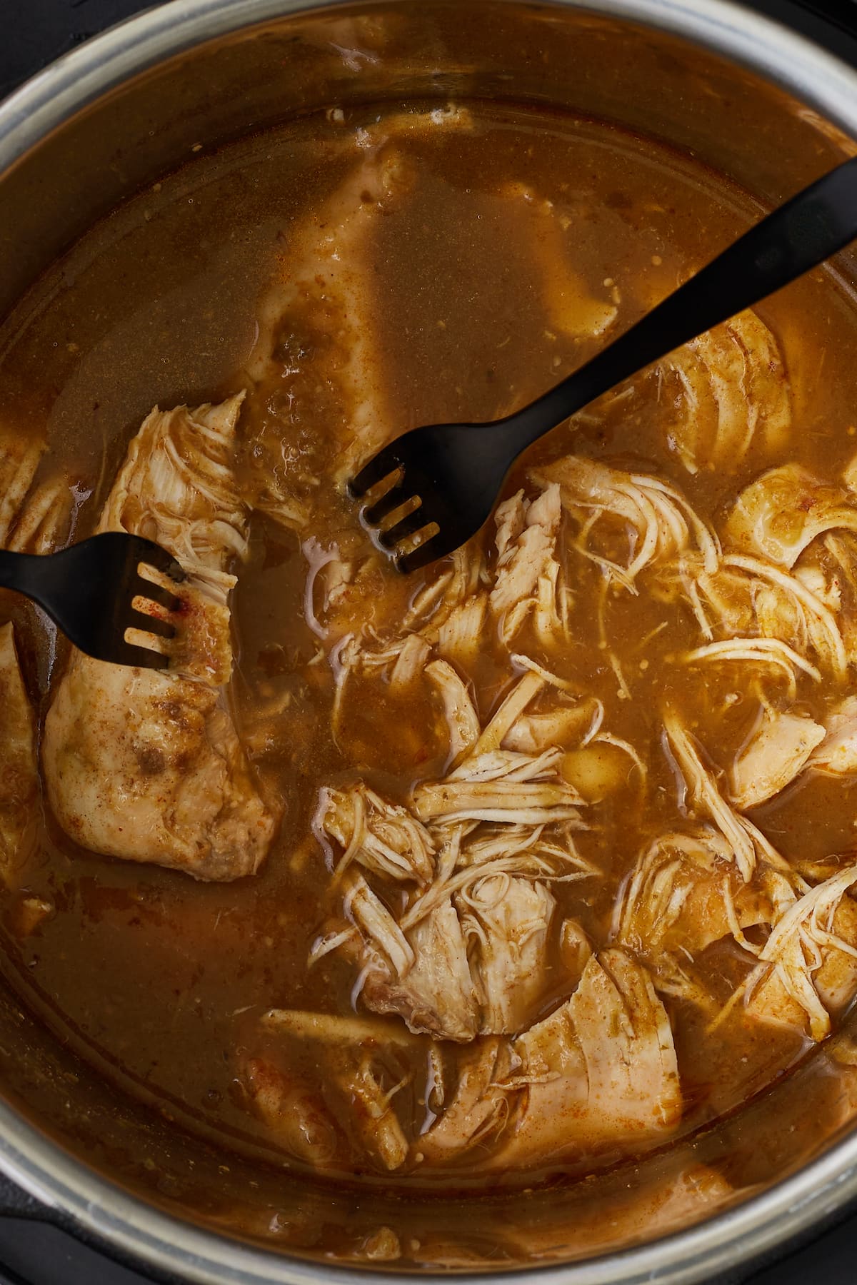 Forks are used to shred the cooked chicken breast into the salsa verde sauce.