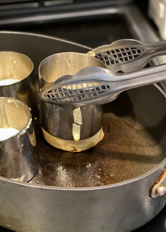 removing the aluminum mold from pancakes in a skillet with metal tongs