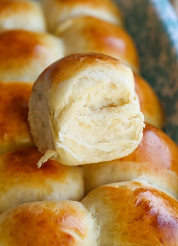 Freshly baked Hawaiian roll on top of a tray of more Hawaiian rolls