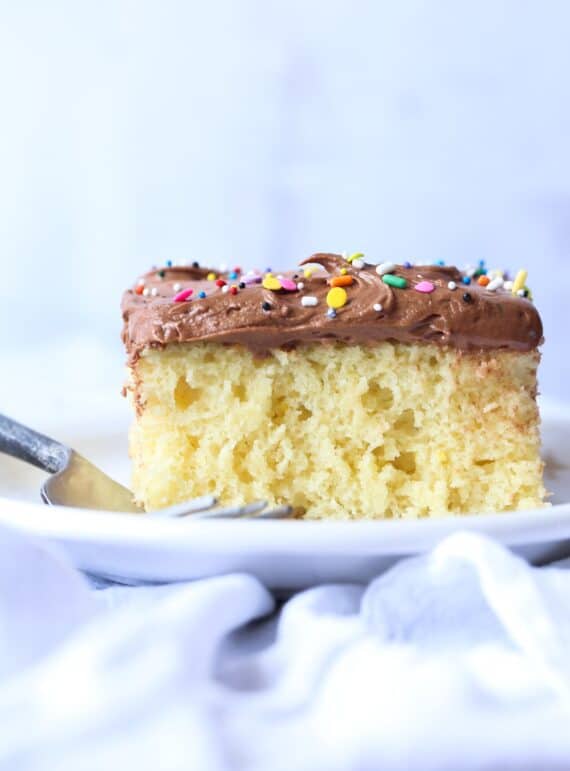 Gâteau à la vanille avec glaçage au chocolat et arrose arc-en-ciel sur une plaque blanche avec une fourchette.