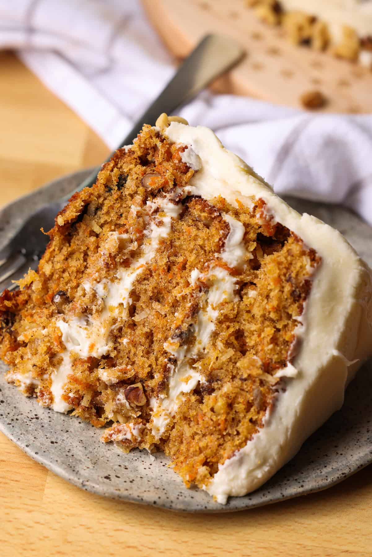 This is the best carrot cake recipe ever! With moist cake filled with pineapple and coconut, smothered with homemade cream cheese frosting. A slice of moist carrot cake with cream cheese frosting on a plate.