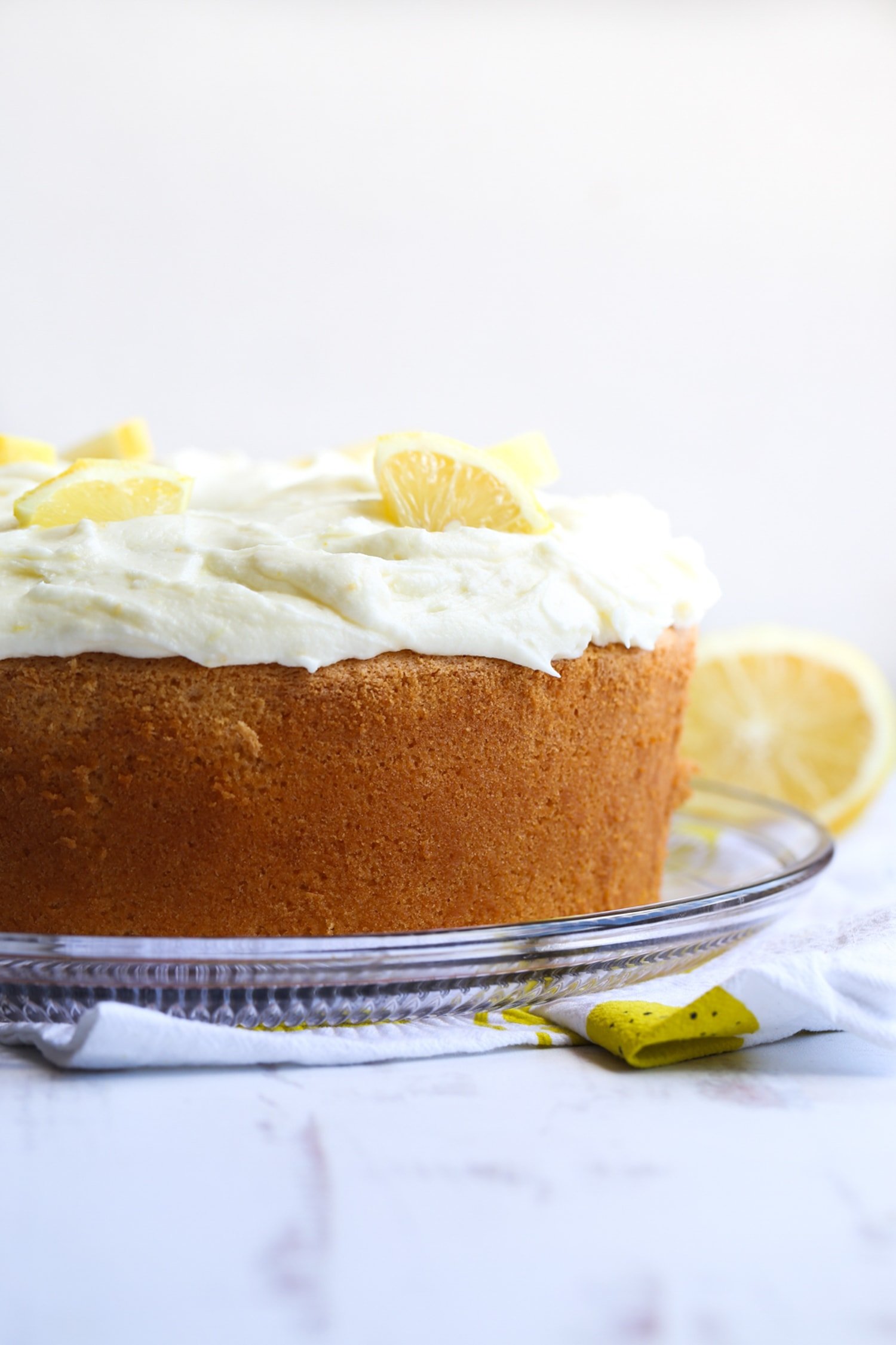 Lemon chiffon cake on a cake plate from the side with fluffy lemon frosting