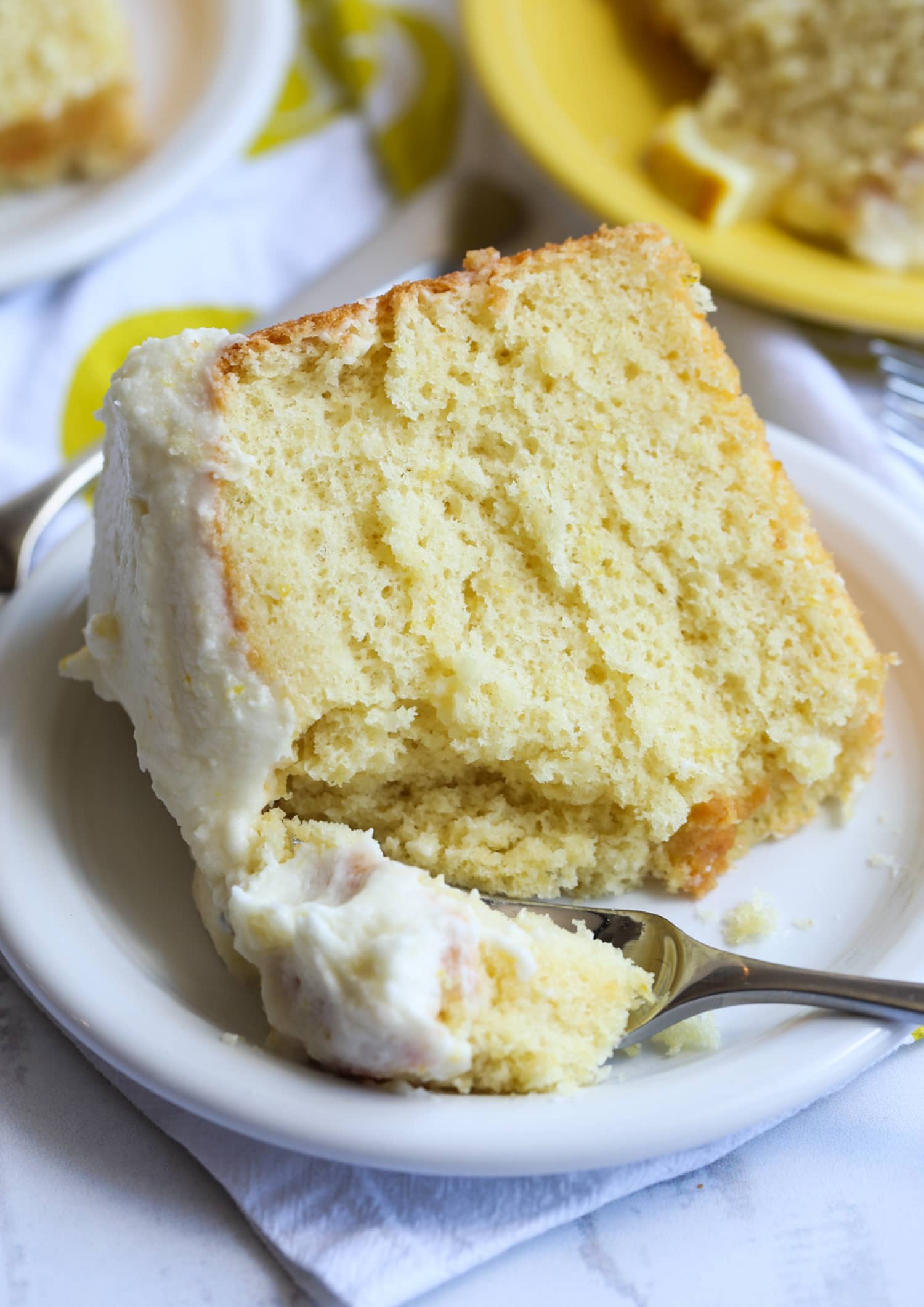 A piece of lemon cake on a plate with a forkful take out