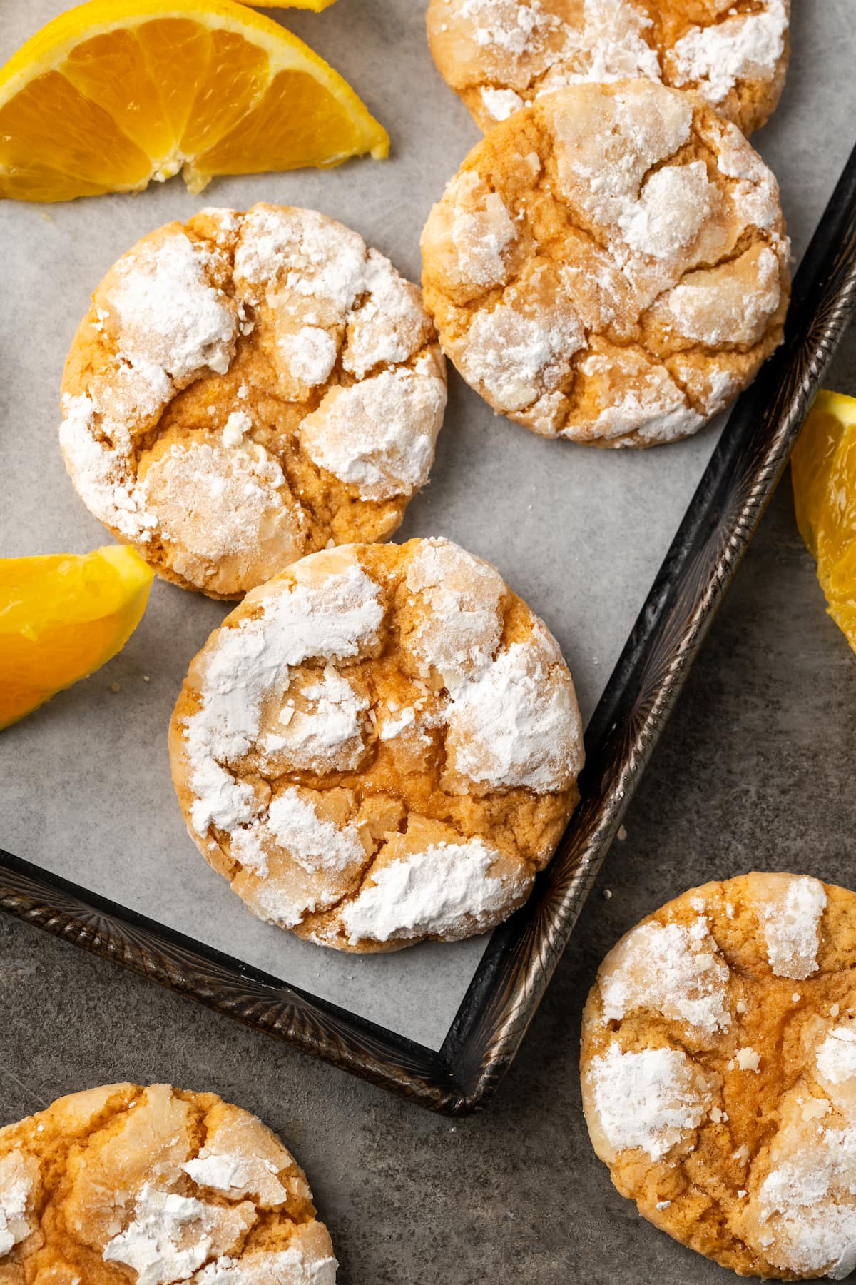Assorted orange crinkle cookies on a lined baking sheet next to orange wedges.