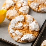 Close up of assorted orange crinkle cookies on a lined baking sheet next to orange wedges.