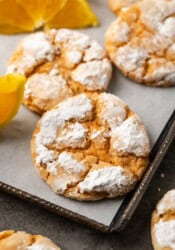 Close up of assorted orange crinkle cookies on a lined baking sheet next to orange wedges.
