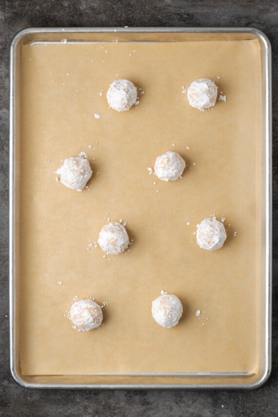 Orange cookie dough balls coated in powdered sugar on a lined baking sheet.