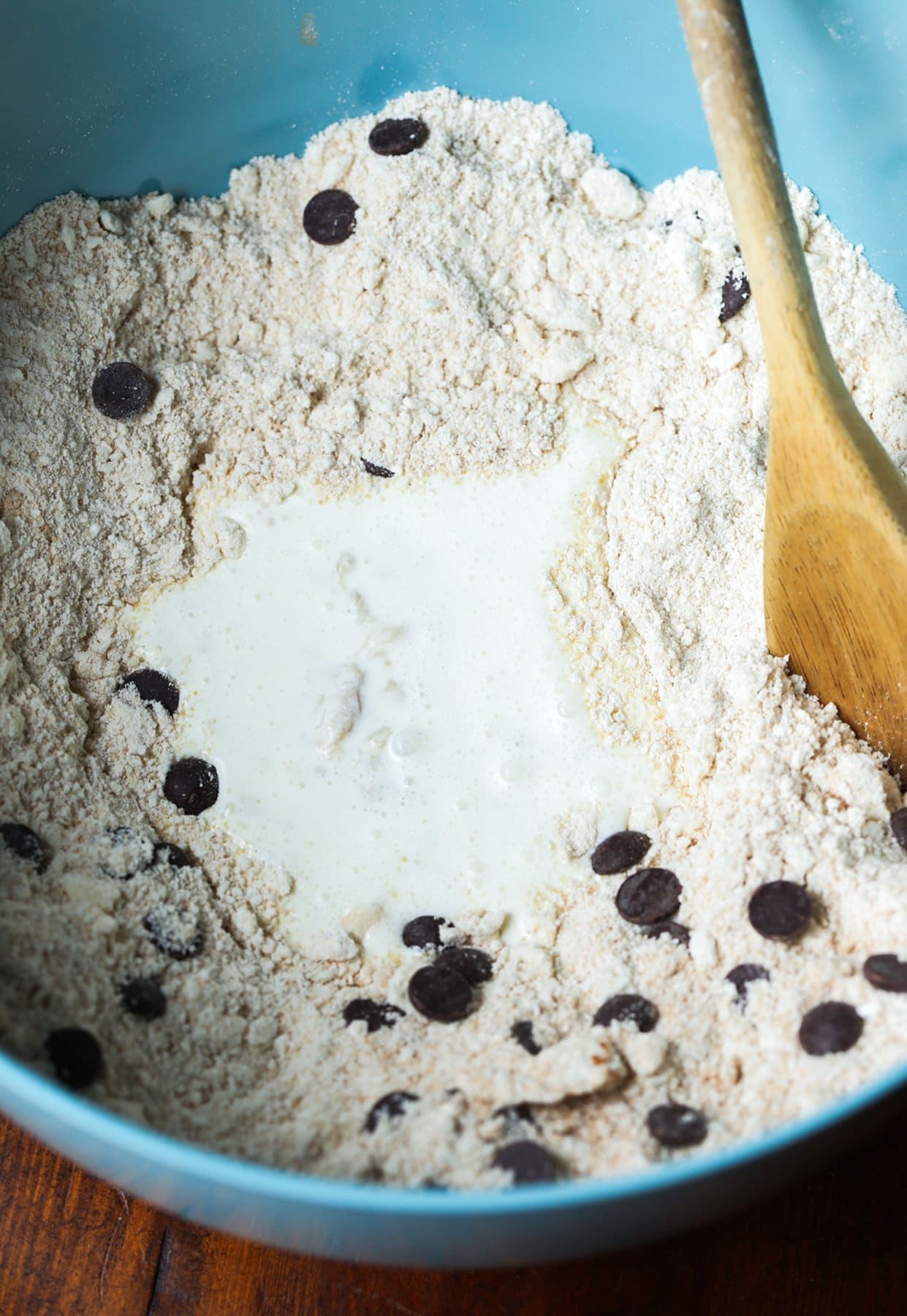 A blue bowl with flour, chocolate chips and heavy cream stirred with a wooden spoon