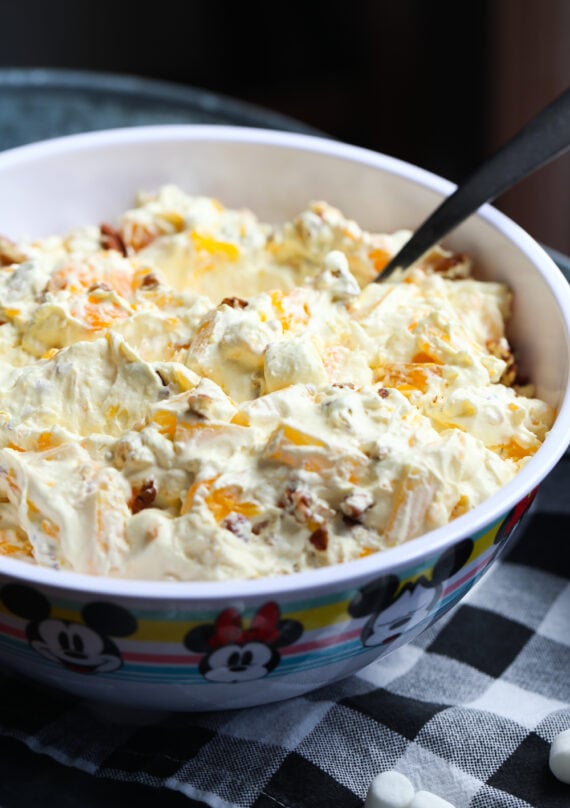 A bowl of orange cream fruit salad topped with chopped pecans ready to be served.