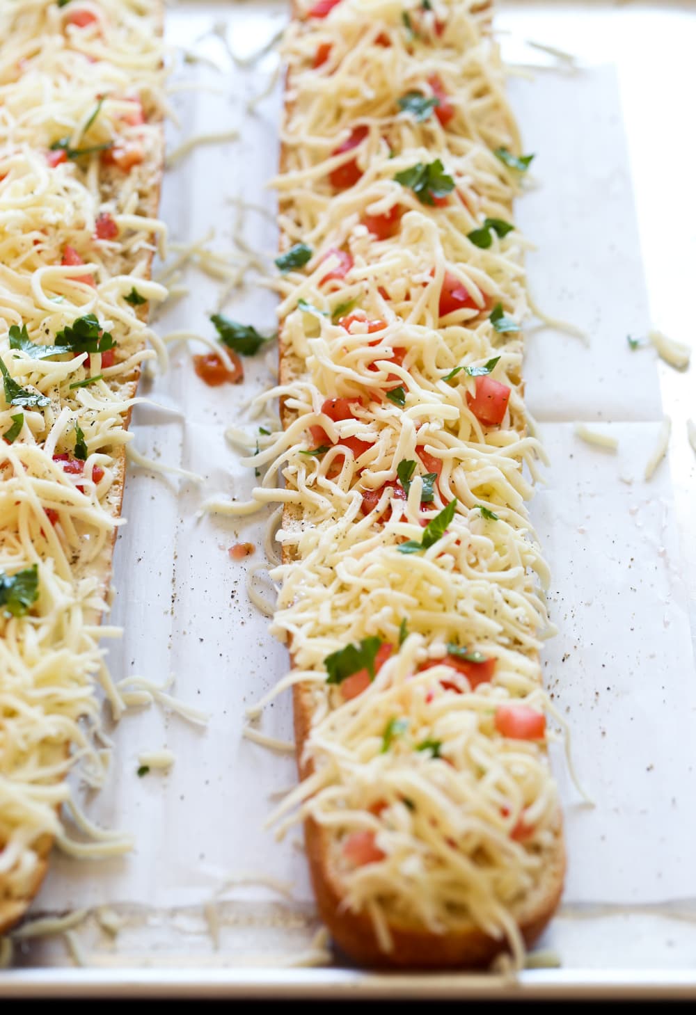 A baguette covered in cheese and tomatoes on a baking sheet