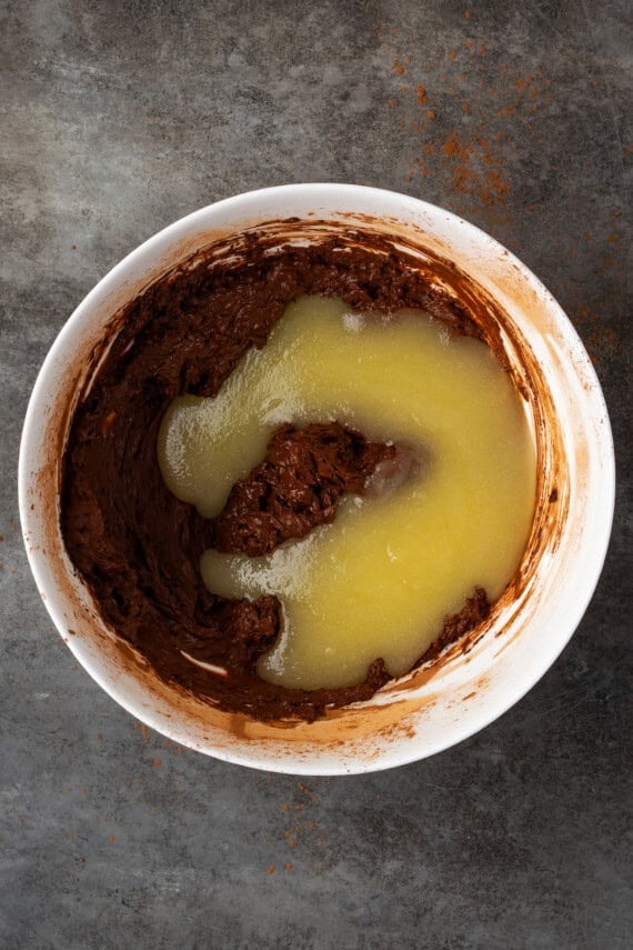 Melted butter mixture added to brownie batter in a white bowl.