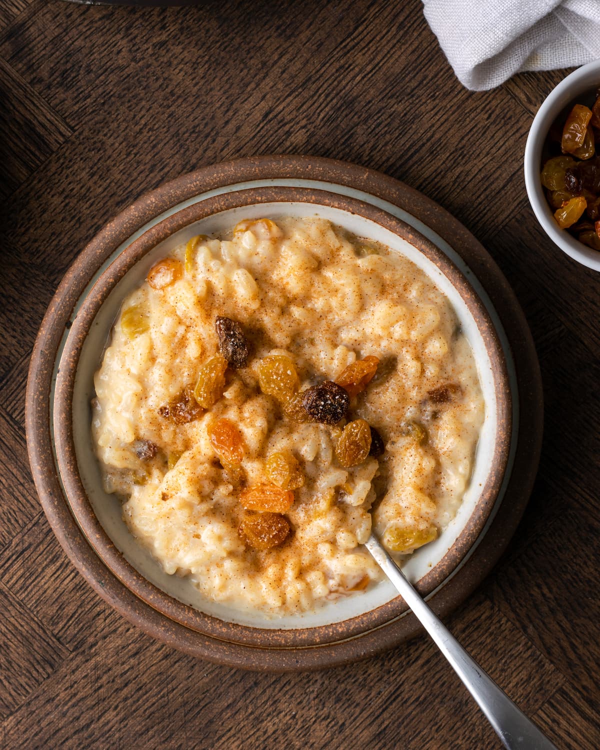 Top view of a bowl of creamy rice pudding topped with raisins, with a spoon.