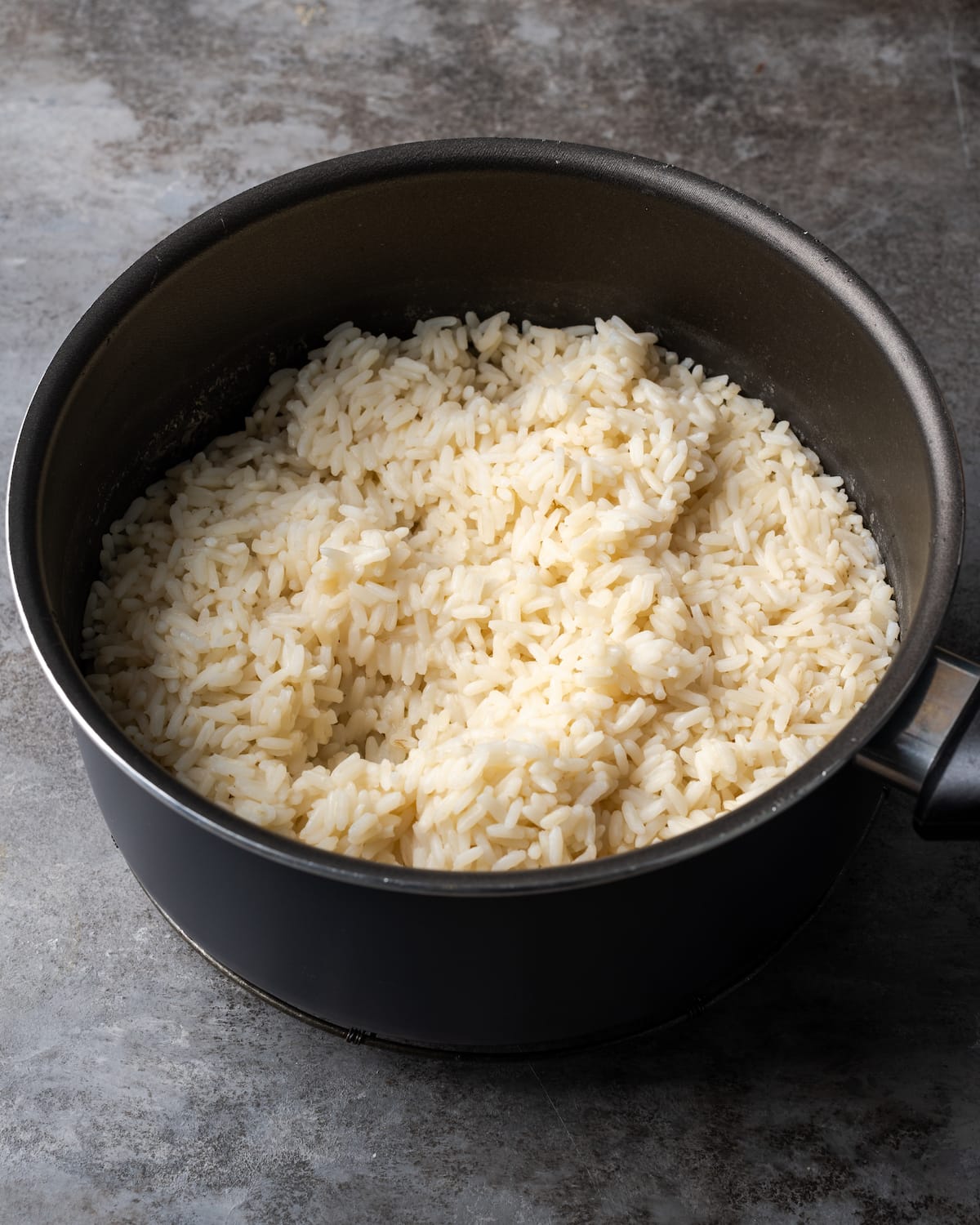 Cooked long grain rice in a black saucepan.