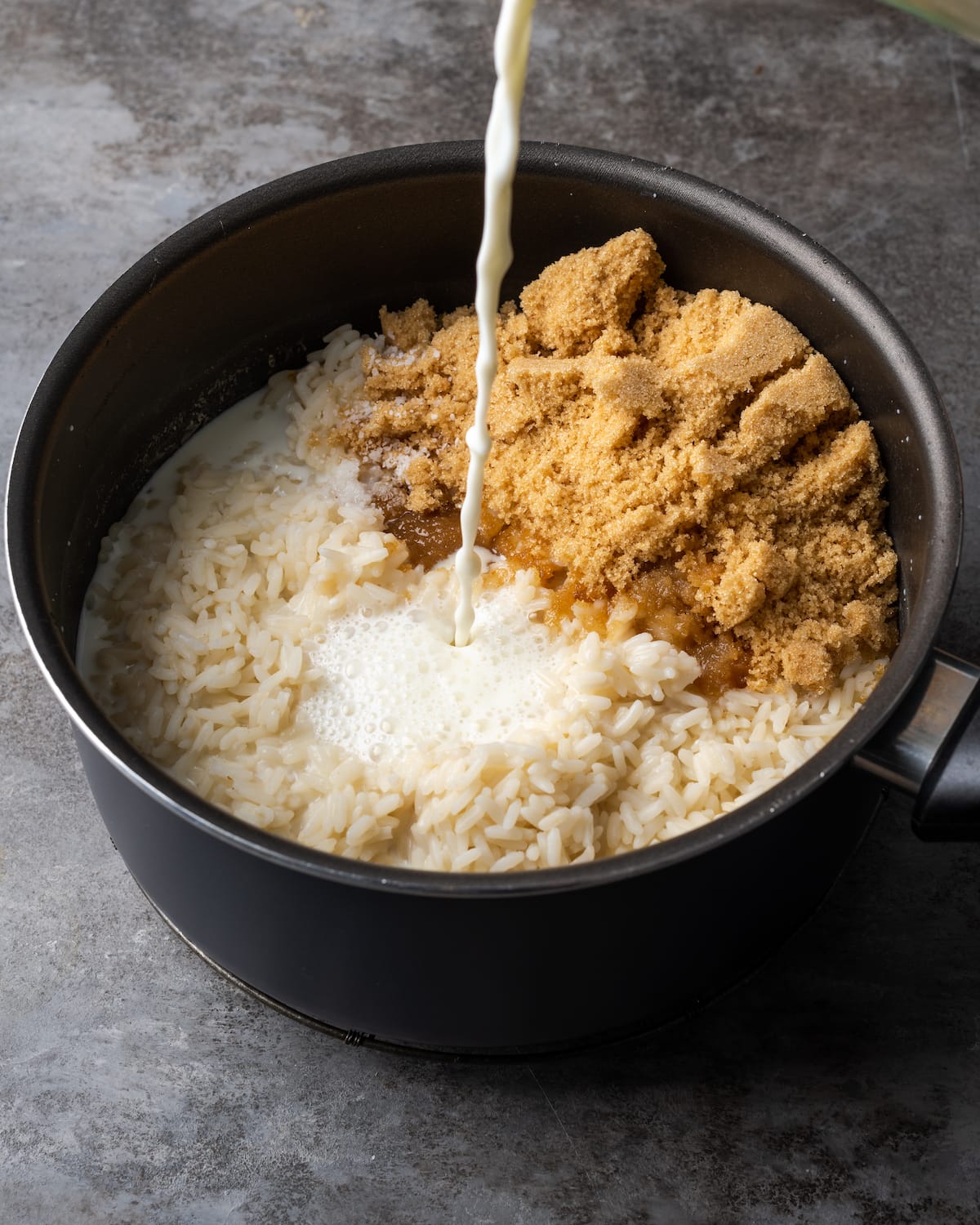 Milk and brown sugar are added into a black saucepan filled with rice.