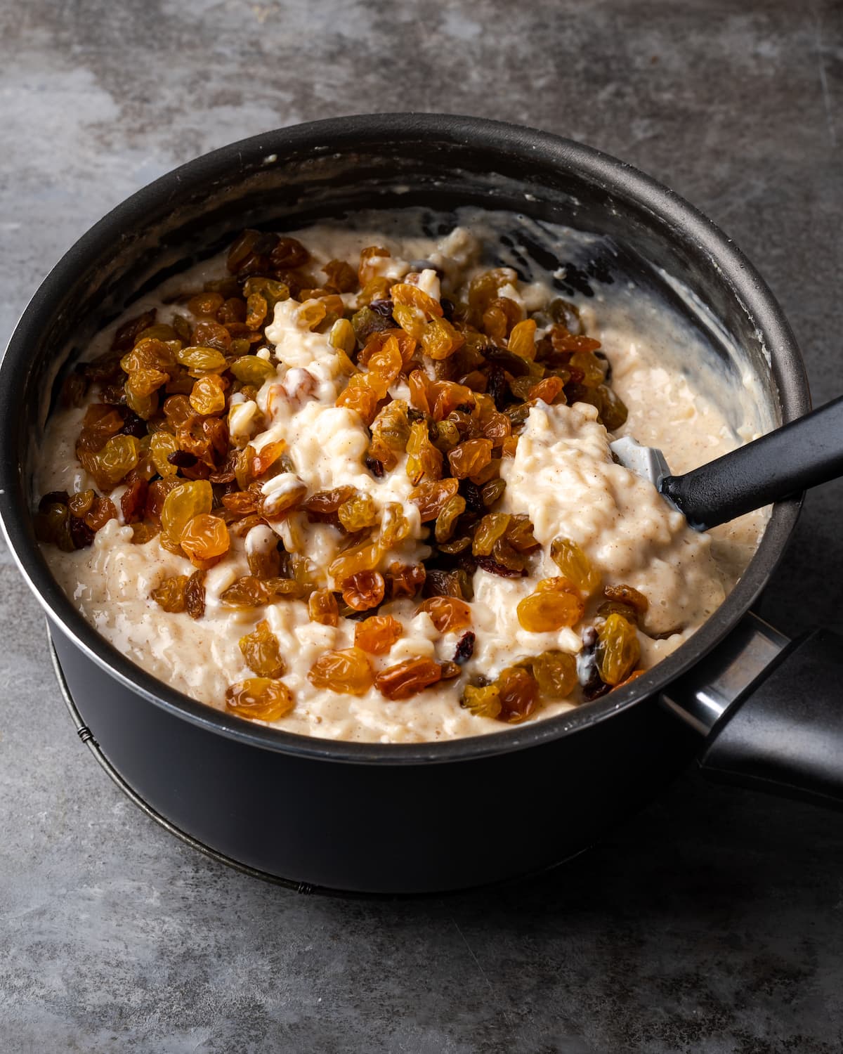 Raisins are stirred into a saucepan filled with rice pudding.