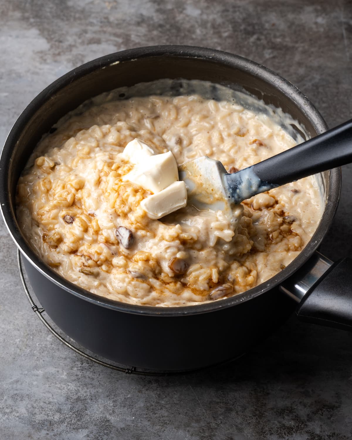 Butter cubes and vanilla extract are stirred into a saucepan filled with rice pudding.