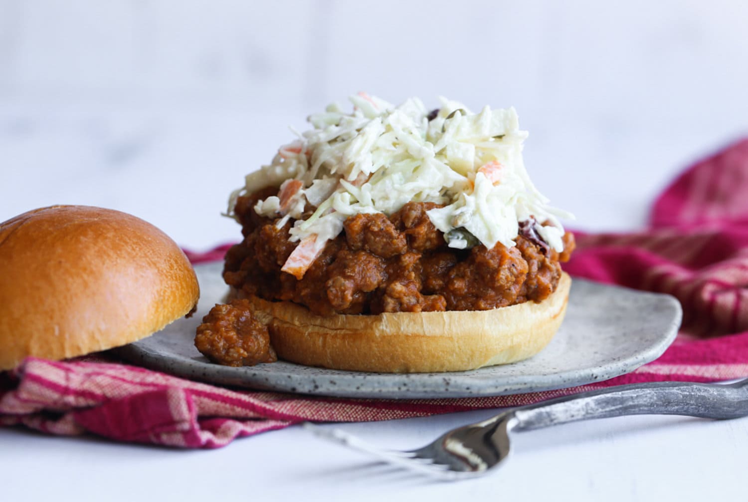 Topping a skoppy joe with cole slaw on a plate