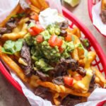 Carne Asada French Fries topped with guacamole, cheese sauce, and sour cream in a basket