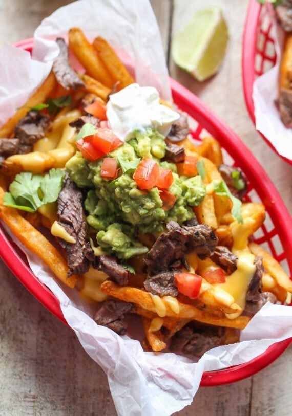Carne Asada French Fries topped with guacamole, cheese sauce, and sour cream in a basket