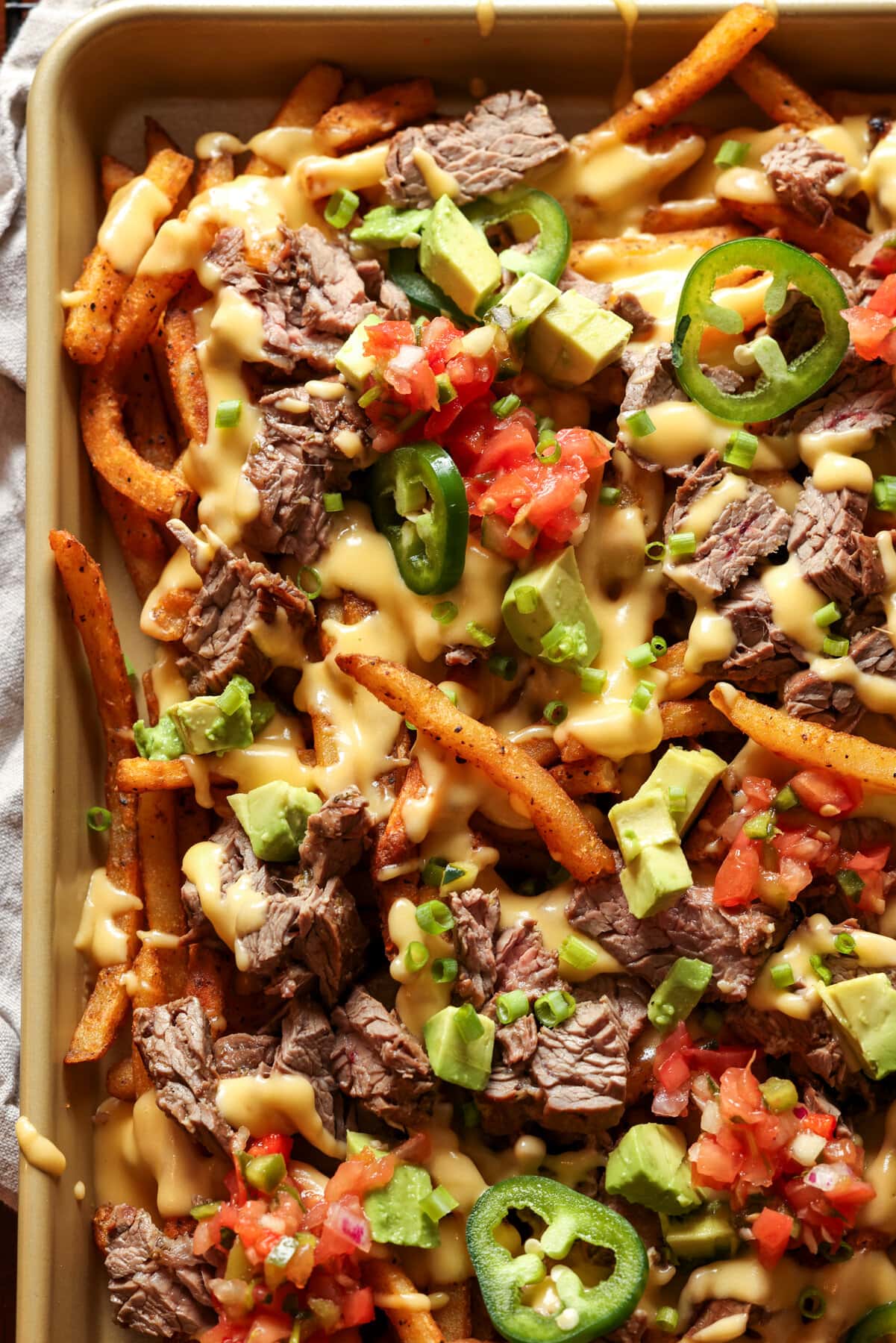 Carne Asada Fries topped with melted cheese and all the fixings on a baking sheet
