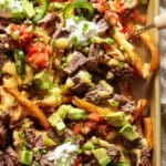 Carne Asada Fries on a large baking sheet topped with sour cream and pico de gallo.