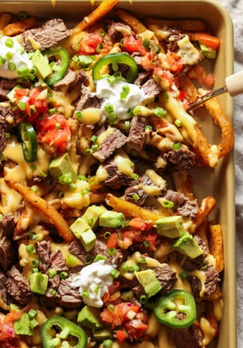 Carne Asada Fries on a large baking sheet topped with sour cream and pico de gallo.