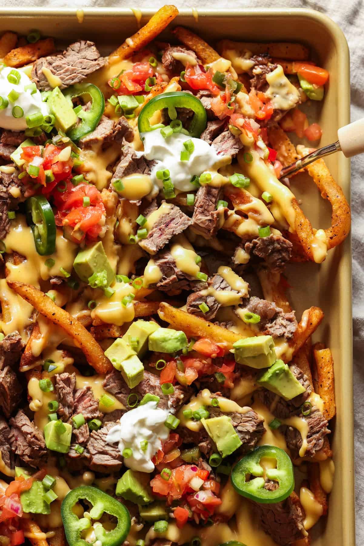 Carne Asada Fries on a large baking sheet topped with sour cream and pico de gallo.