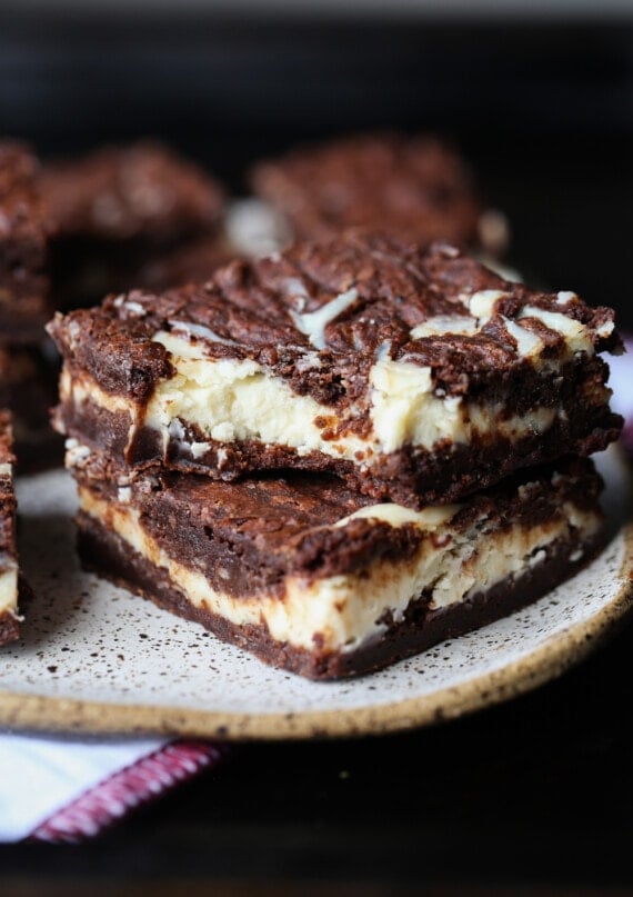 Two Cheesecake Brownies Stacked on a Plate With a Bite Taken From the Top One