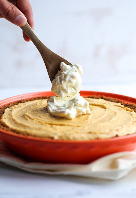 A Pumpkin Mousse Pie with a Dollop of Whipped Cream Being Added on Top with a Wooden Spoon