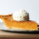 A slice of sweet potato pie topped with a dollop of whipped cream