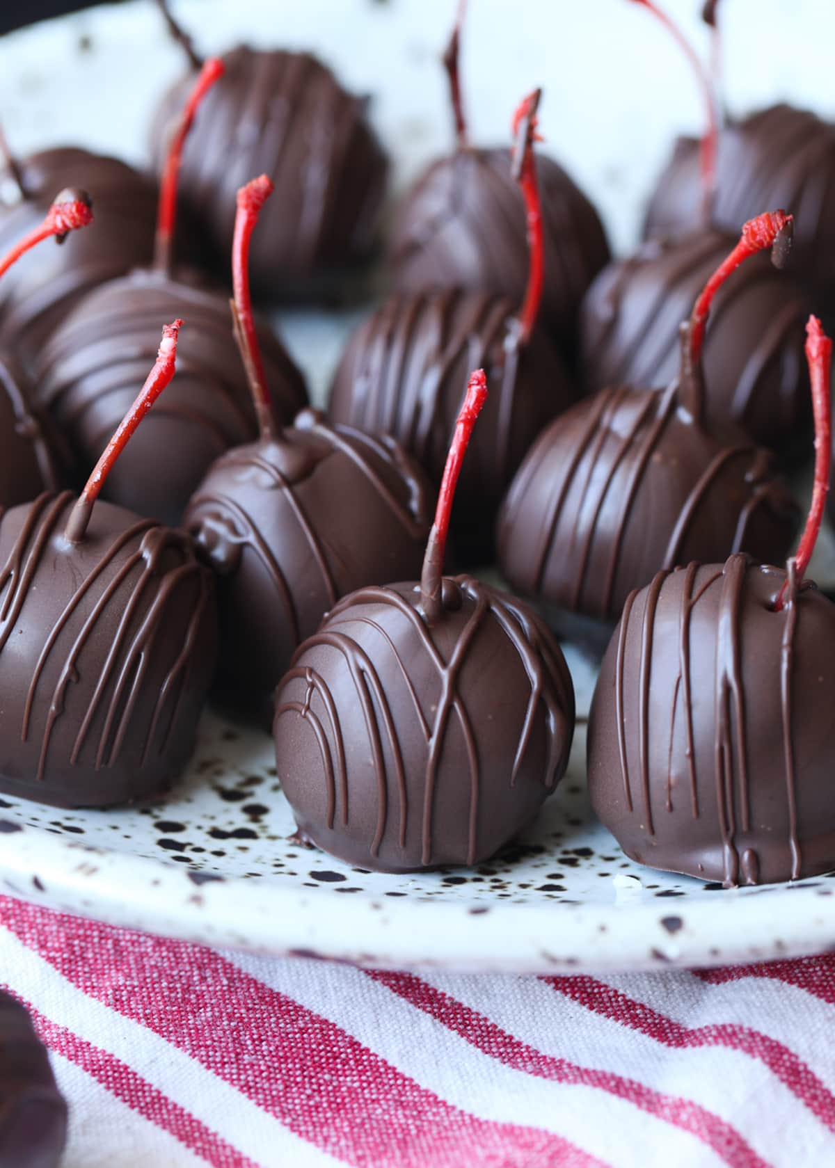 Chocolate covered cherries on a stoneware plate with the red stems peeking out the top.