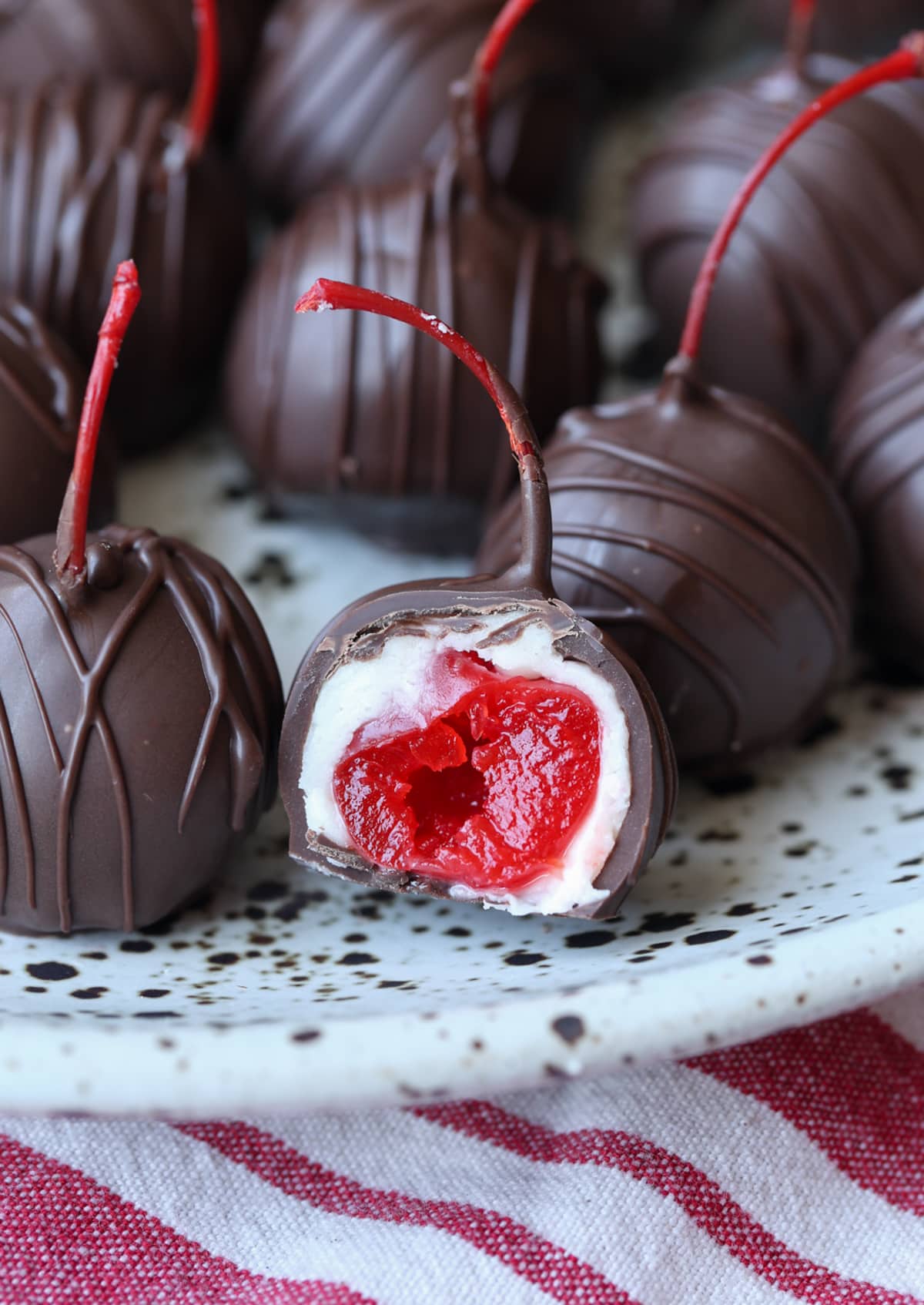A chocolate covered cherry bitten in half on a plate showing the cherry, white sugar coating and chocolate shell.