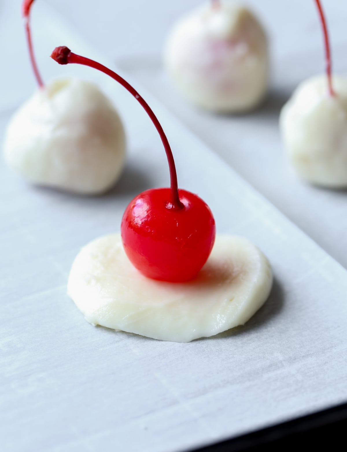 A red Maraschino cherry on a disc of fondant before being coated.