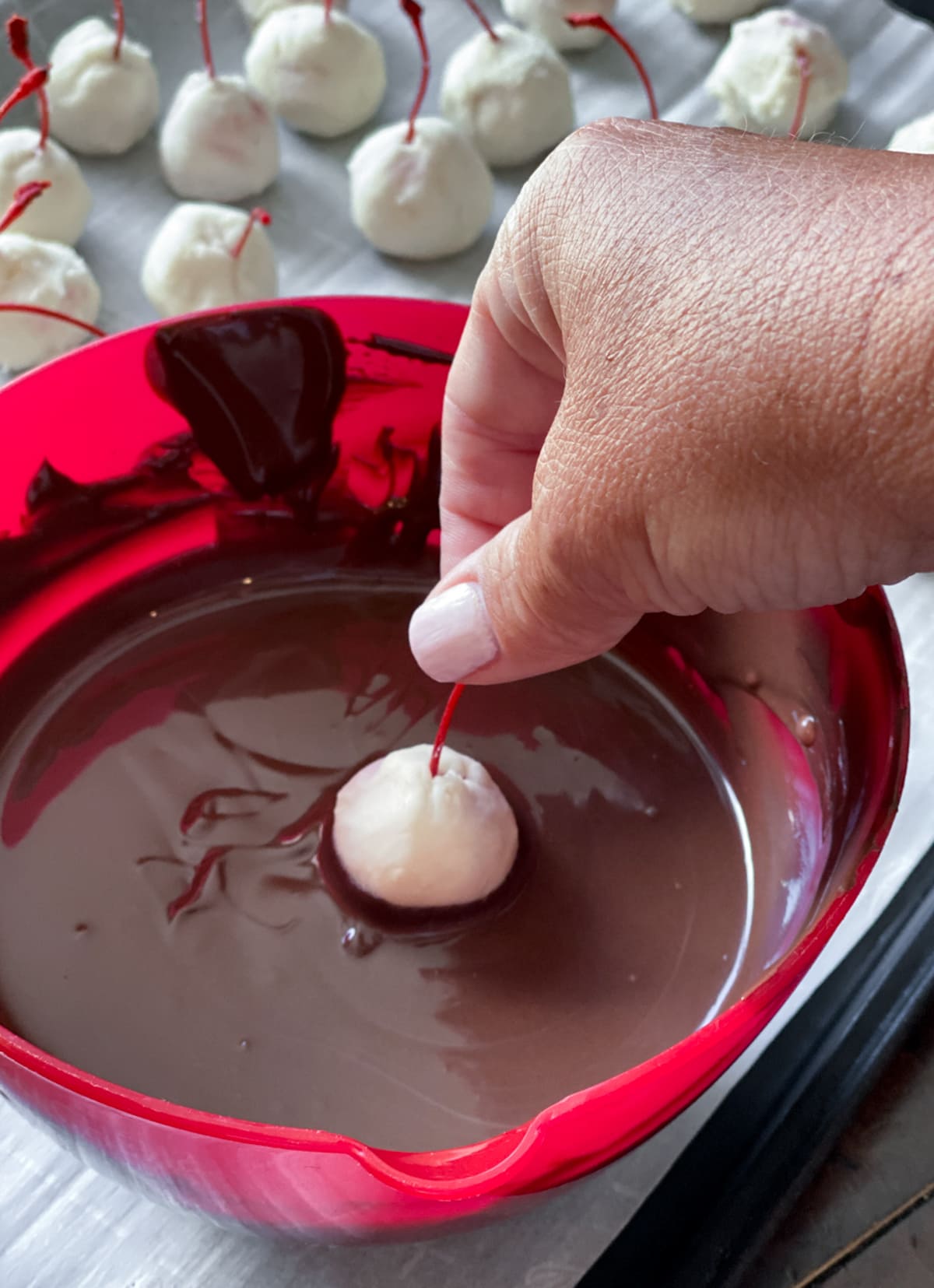 A cherry covered in white fondant being dipped into melted chocolate