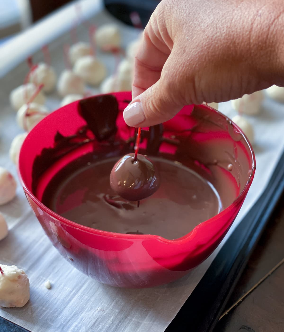 DIpping a cherry into melted chocolate in a red bowl.