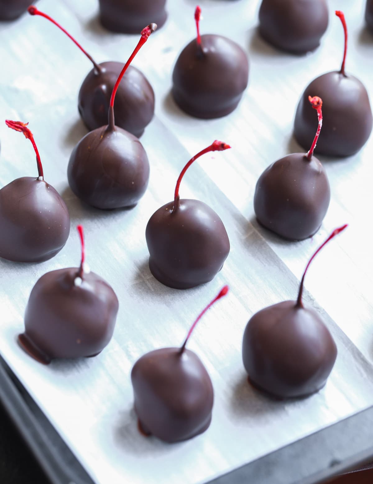 Freshly dipped chocolate cherries on parchment paper.