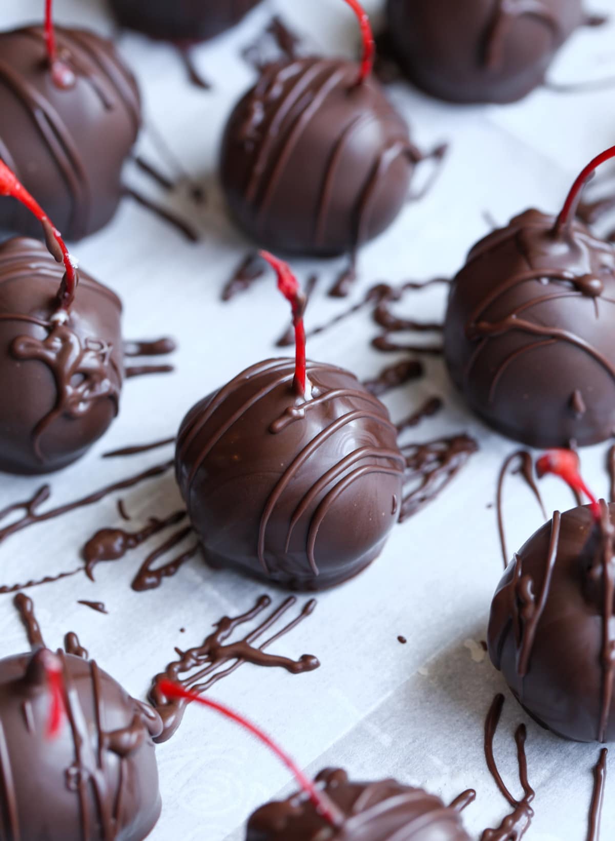 Chocolate covered cherries on a parchment lined baking sheet with drizzled chocolate.