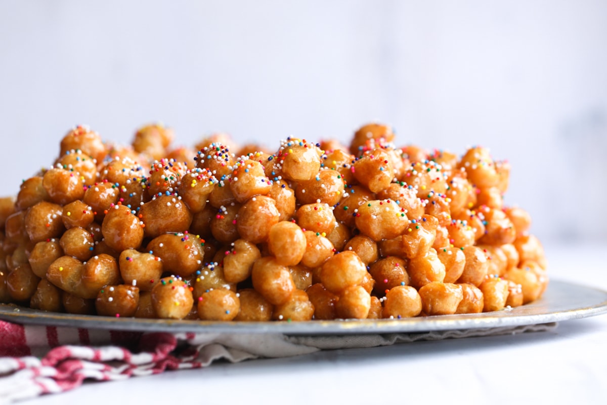 Struffoli honey balls on a silver serving plate topped with nonpareil sprinkles
